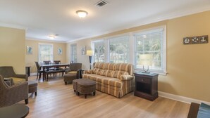A living room with a sofa, ottoman, dining table, chairs, and a lamp.