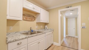 A kitchen with white cabinets, a granite countertop, a coffee maker, and a sign that says "This kitchen is seasoned with love."