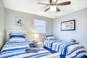 A bedroom with two beds, a ceiling fan, and artwork on the walls.