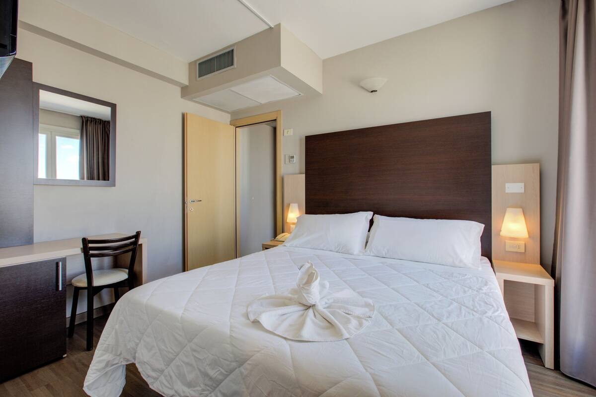 Una habitación de hotel con una cama grande, un escritorio, una silla y un espejo.