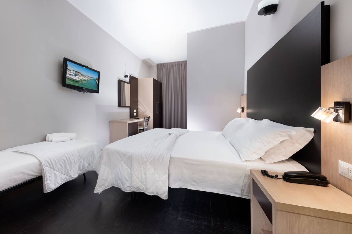 Habitación de hotel con dos camas individuales, un televisor montado en la pared, un escritorio con teléfono y un espejo.