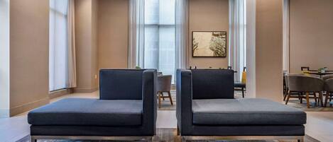 Un vestíbulo de hotel moderno con dos sofás grises, una zona de comedor y un cuadro abstracto grande en la pared.