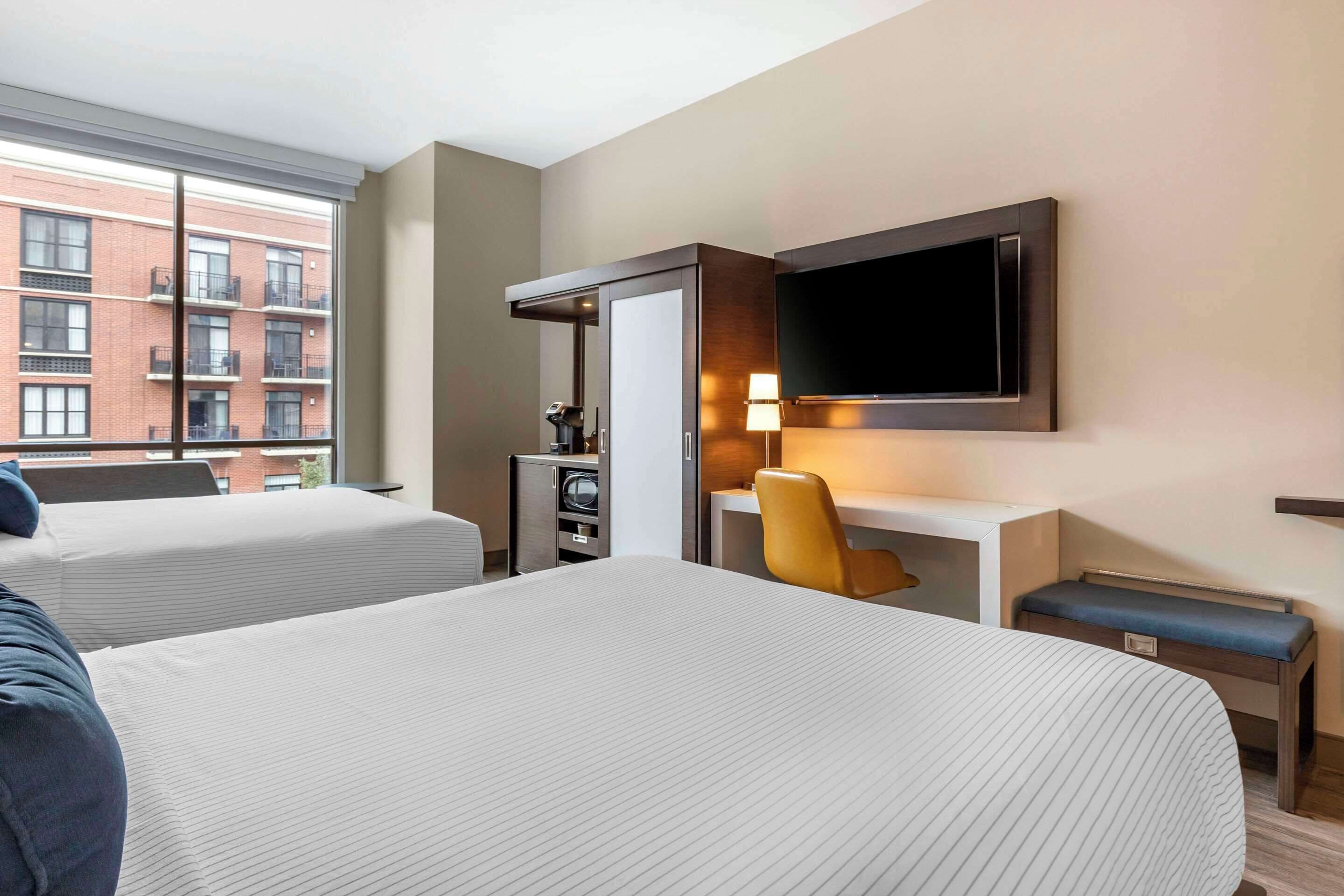 A hotel room with two beds, a desk, a chair, a TV, and a minibar.