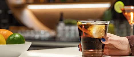 Eine Bar mit einem Glas dunklem Getränk, einem Limettenschnitz und einer Obstschale.