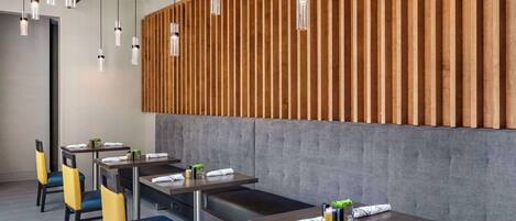 Un comedor moderno con listones de madera, asientos tapizados en gris e iluminación colgante.