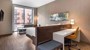 Habitación de hotel con cama, escritorio, silla, una mesita y un cuadro en la pared.