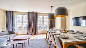 Un espace repas moderne avec une longue table dressée pour six personnes, un canapé et un téléviseur fixé au mur.