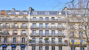 Un immeuble à plusieurs étages doté de balcons, une enseigne indiquant « PARC EMERGE », et un arbre au premier plan.