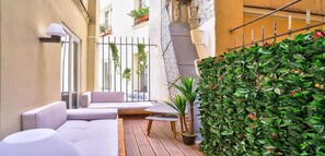 A narrow outdoor space with a white sofa, a small table, and a potted plant.