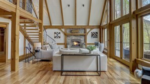 A spacious living room with a fireplace, wooden beams, and large windows.