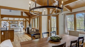 A spacious living area with a wooden ceiling, a fireplace, and large windows offering a view of the outdoors.