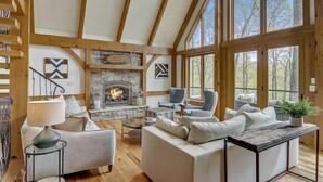 A spacious living room with a fireplace, wooden beams, large windows, and comfortable seating.