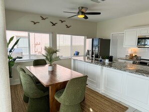 A kitchen with a dining area, white cabinetry, a ceiling fan, and a view through the windows.
