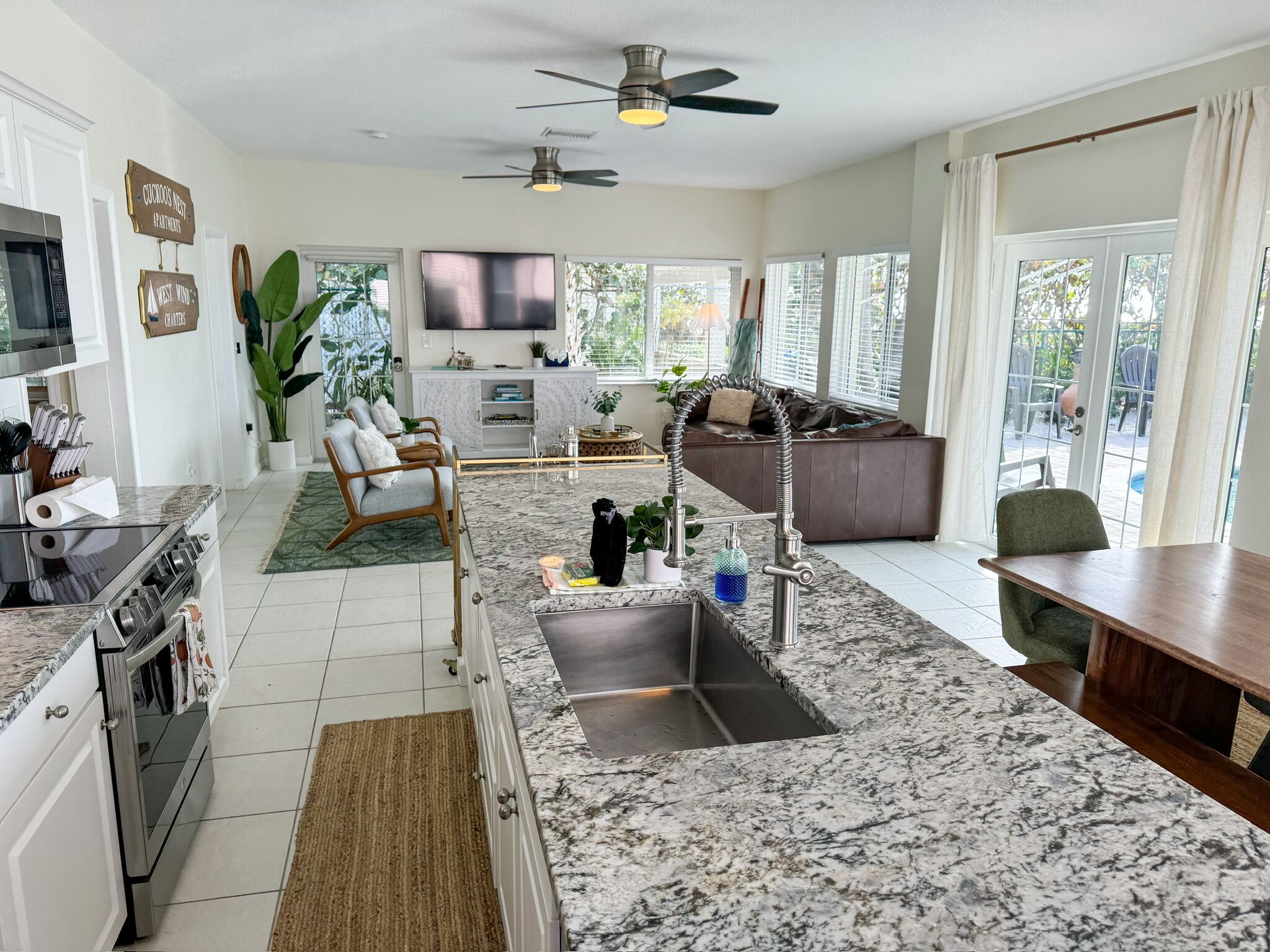 A modern kitchen with a central island, a dining area with a wooden table, and a living space with a sofa and a TV.