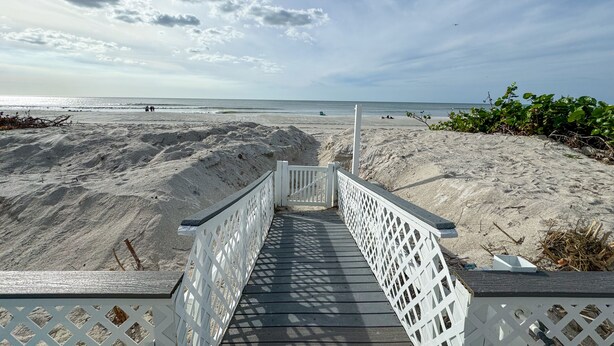 A wooden boardwalk leading to a sandy beach with a clear sky.