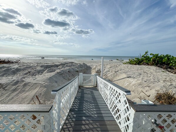 A wooden boardwalk leading to a sandy beach with a clear sky.