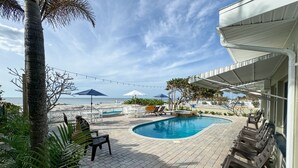 A pool area with lounge chairs, umbrellas, and a view of the beach.