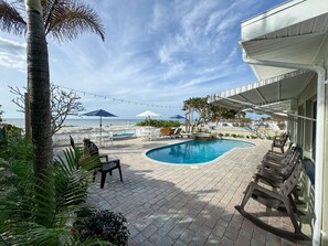 A pool area with lounge chairs, umbrellas, and a view of the beach.