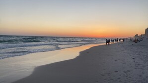 Ein Strand mit Wellen im Sonnenuntergang, Menschen die spazieren gehen und Gebäude im Hintergrund.