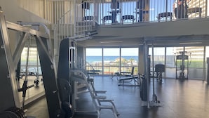 Ein Fitnessstudio mit Gewichthebern, Bänken und Blick auf das Meer durch große Fenster.