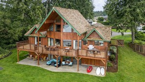 A two-story wooden cabin with a balcony, outdoor seating, and a small boat.