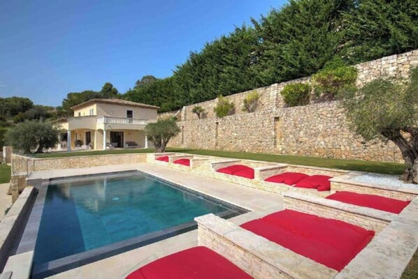 A swimming pool with red cushions, a stone wall, and a building in the background.