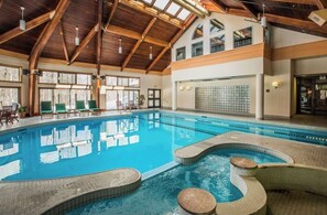 A large indoor swimming pool with a wooden ceiling and multiple windows.