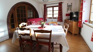 Ein Esszimmer mit einem runden Tisch, Stühlen, einer roten Tischdecke, einem Blumentopf und einem Fernseher auf einer Holzkommode.