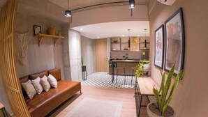 A modern living room with a sofa, a coffee table, and a dining area with a plant. - PRIME LOCATION / Mosaic Studios Barranquilla P-1 (Barranquilla)