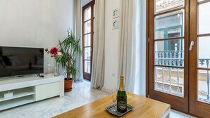 Un salon avec une télévision, une plante en pot, une bouteille de champagne et un balcon doté d’une rambarde.