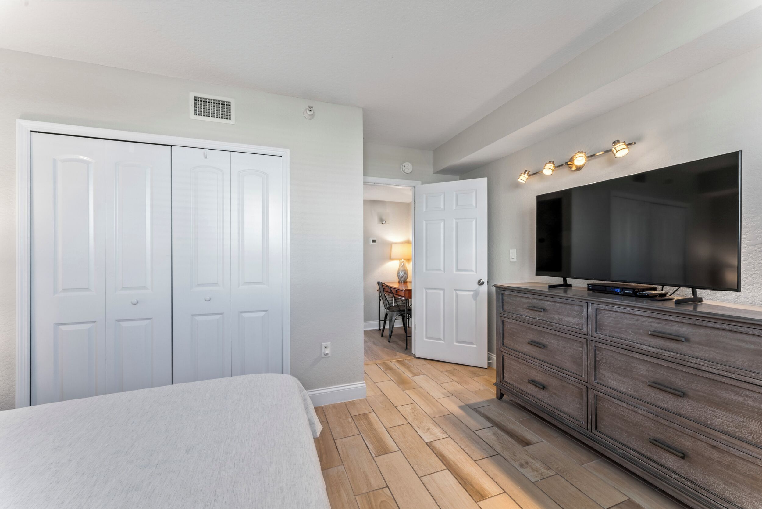 Une chambre à coucher comprenant un lit, une commode, un téléviseur et un couloir menant à une salle à manger.