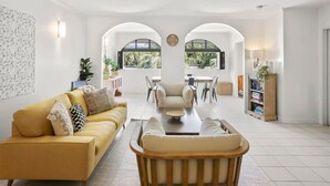 A modern living room with a yellow sofa, a wooden chair, a coffee table, and a dining area with a table and chairs.
