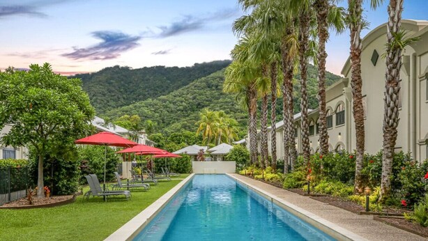 A swimming pool with a view of a lush green hillside, palm trees, and a building with a light-colored facade.