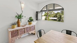 A dining area with a wooden table, black chairs, a decorative cabinet with plants, and a window with an arched top.