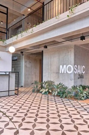 Un intérieur moderne avec un sol à motifs géométriques, un escalier apparent et un mur sur lequel on peut lire le texte « MOSAIC Studios ».