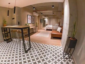 Una habitación de hotel moderna con suelo de diseño geométrico, una mesa de comedor de madera, un sofá y una cama.
