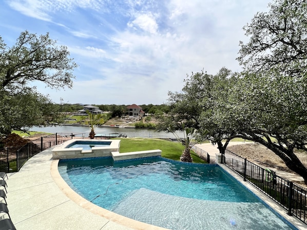 A swimming pool with a curved edge, surrounded by a black metal fence and a grassy area.