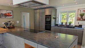 A modern kitchen with a central island, built-in appliances, and a view of greenery outside. - Unique, Spacious, Self-Built Eco House with Huge Garden and Movie Room (Andover)