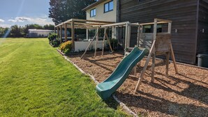 A backyard with a wooden play structure, including a slide, and a greenhouse. - Unique, Spacious, Self-Built Eco House with Huge Garden and Movie Room (Andover)