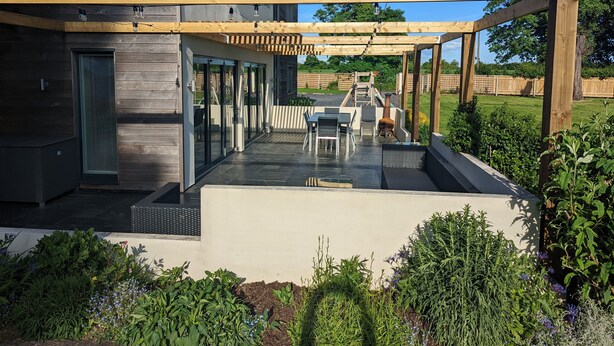 A modern outdoor patio with a pergola, a dining area, and a barbecue grill. - Unique, Spacious, Self-Built Eco House with Huge Garden and Movie Room (Andover)