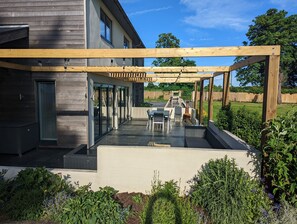 A modern outdoor patio with a pergola, a dining area, and a barbecue grill. - Unique, Spacious, Self-Built Eco House with Huge Garden and Movie Room (Andover)