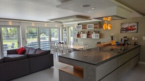 A modern kitchen with a central island, dining area with chairs, and a sofa with a red pillow. - Unique, Spacious, Self-Built Eco House with Huge Garden and Movie Room (Andover)