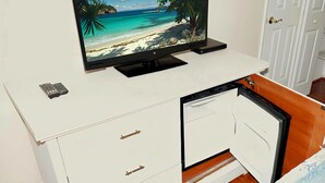 A white entertainment unit with a flat-screen TV displaying a beach scene, a small remote, and a drawer with a cabinet door.