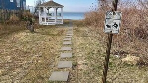 A gazebo with a clear view of the ocean, a stone pathway leading to it, and a 'Dog Waste' sign.