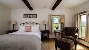 A bedroom with a bed, two bedside tables, a chair, a window with curtains, and a decorative wall piece. - Forest Suite - 2 OR 3 Rooms + Bath (Keene)