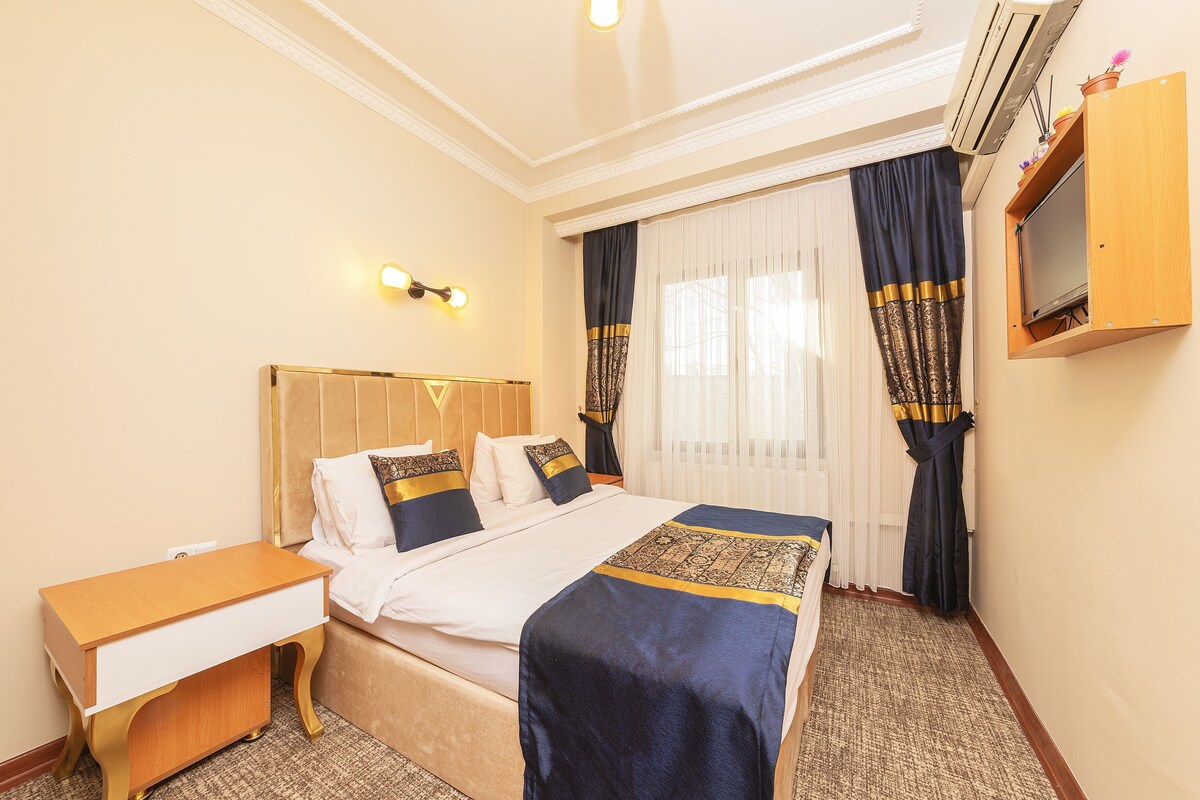 A hotel room with a bed, bedside table, TV, and curtains.