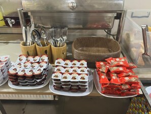 Zona de bufé con bandejas de comida, utensilios y condimentos.