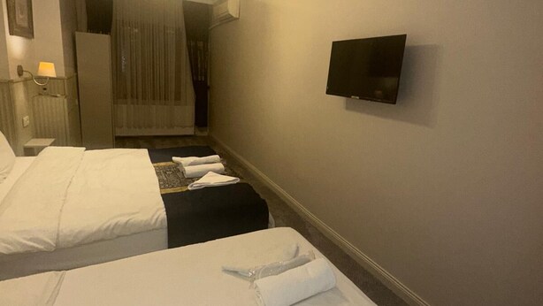 A hotel room with two beds, a television on the wall, a ceiling fan, and a window with curtains.