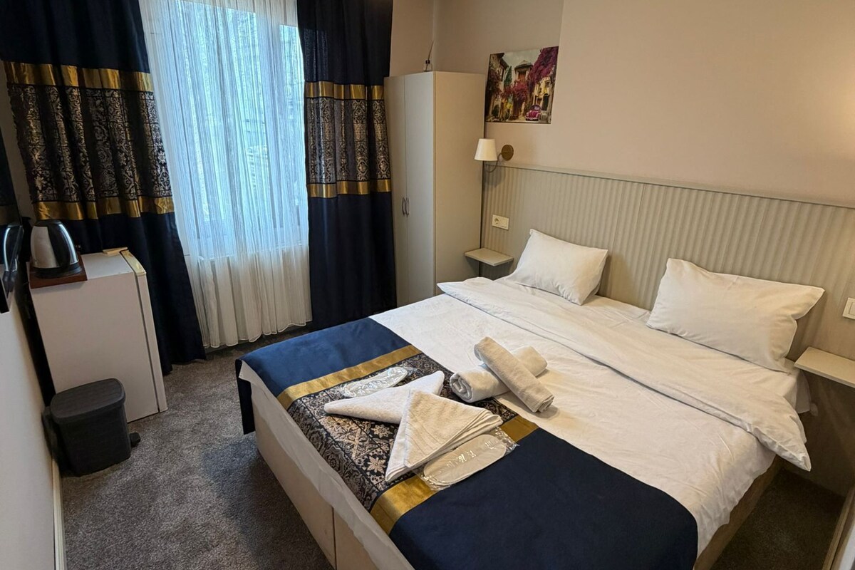 A hotel room with a bed, bedside table, lamp, and a painting on the wall.