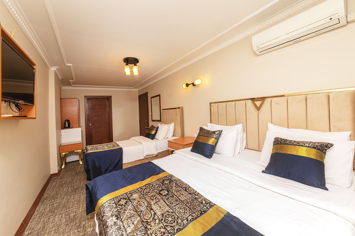 A hotel room with two beds, a desk, a chair, an air conditioner, and a mirror.